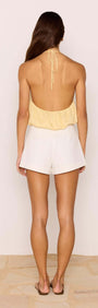 Back view of a model wearing the Butter Yellow Halter-Neck Low Back Bubble Top with white shorts.