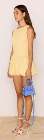 Model wearing a Butter Yellow Shirred Bubble Mini Dress paired with a blue handbag, showcasing a fun summer look.