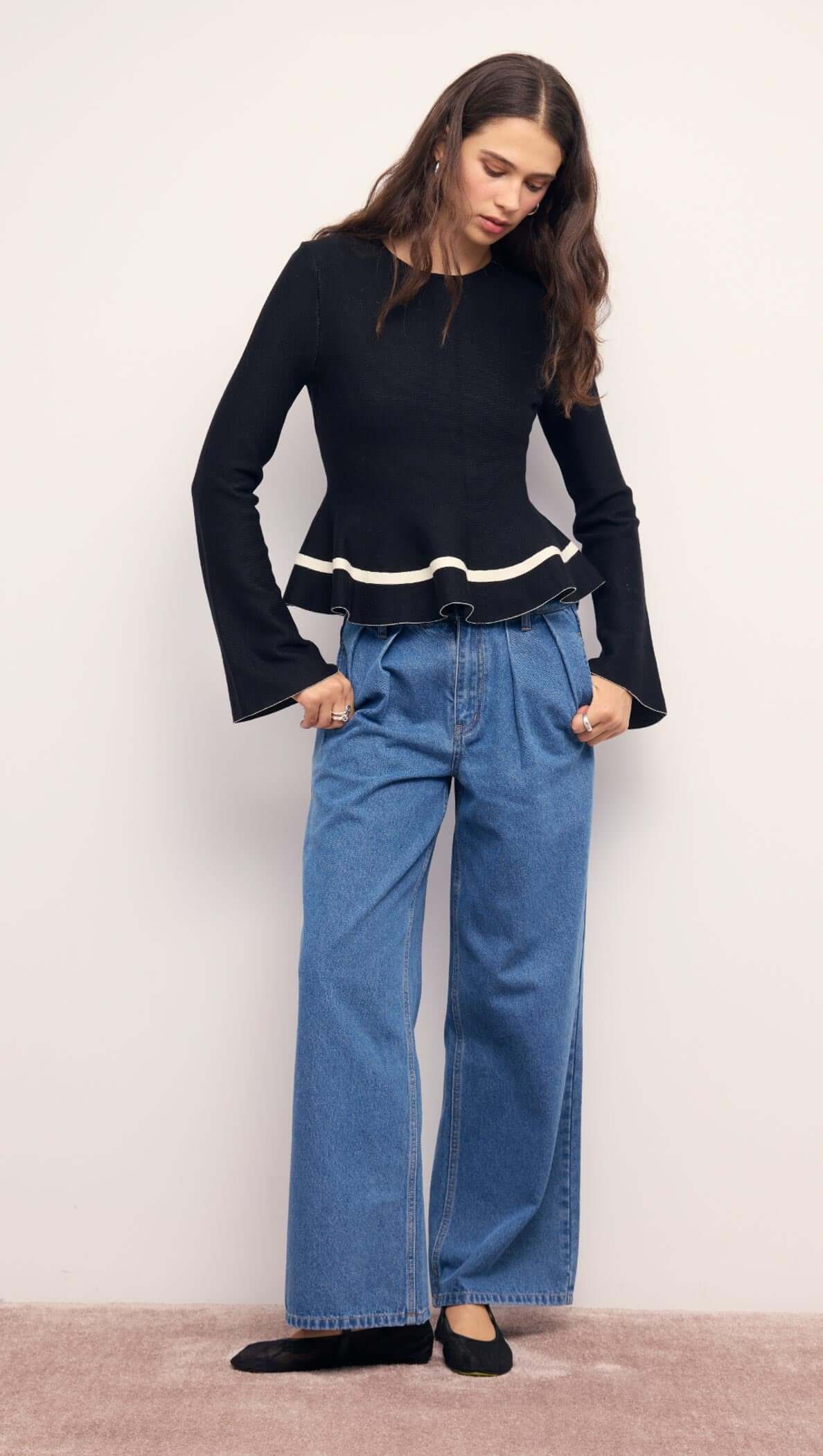 Model wearing a Black Peplum Knit Top With Contrast Trim paired with wide-leg jeans.