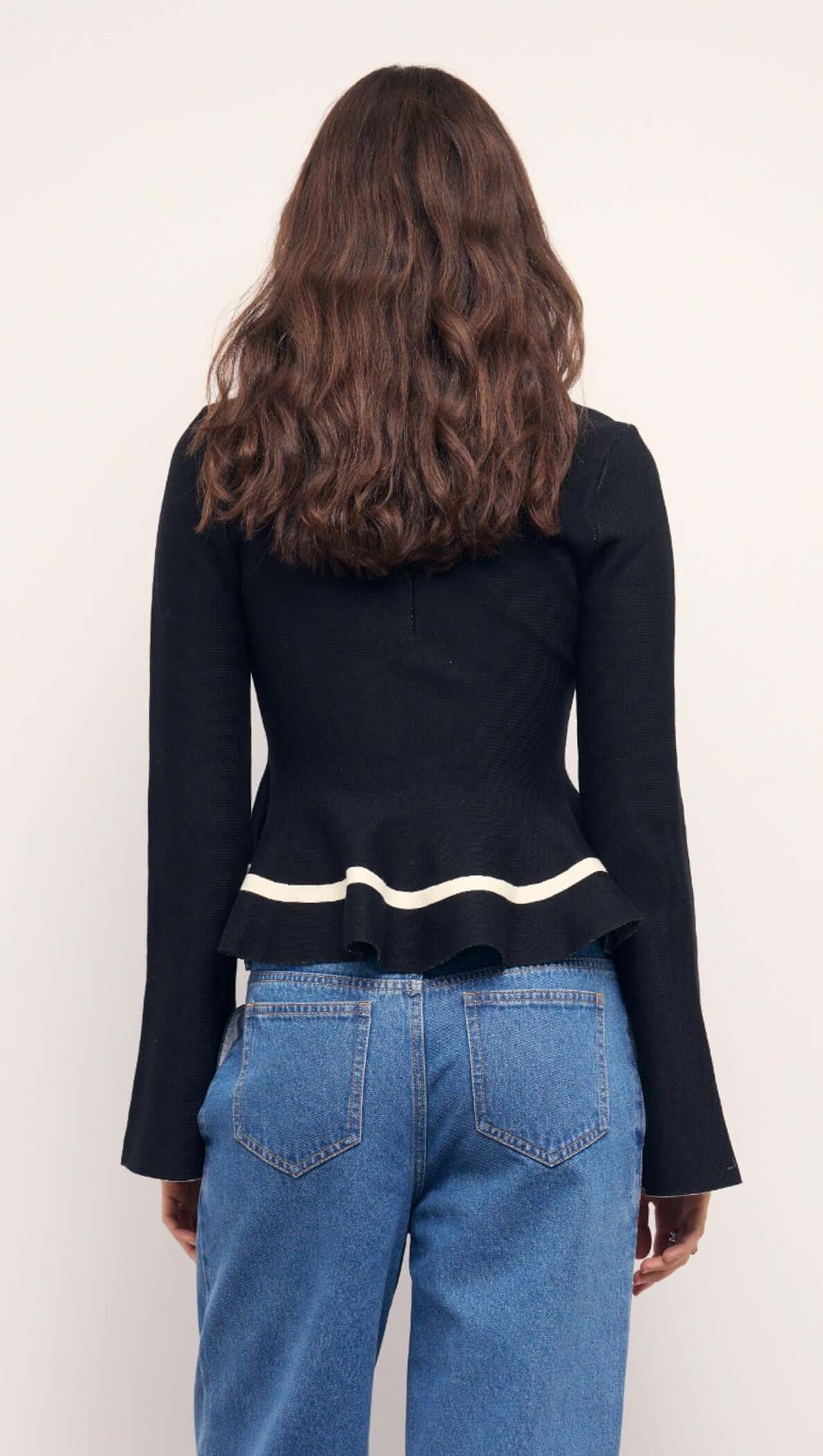 Back view of a model wearing a Black Peplum Knit Top With Contrast Trim and high-waisted jeans.