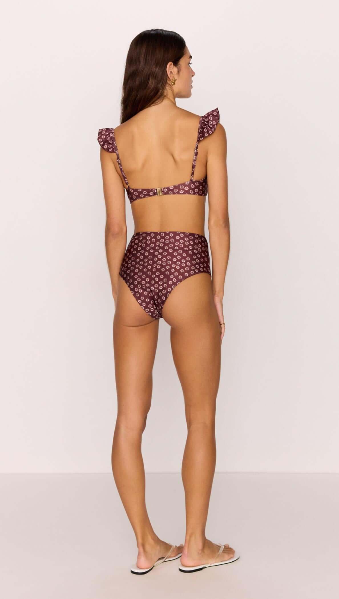 Back view of a woman wearing a burgundy floral print high-waisted bikini pant with ruffled straps.