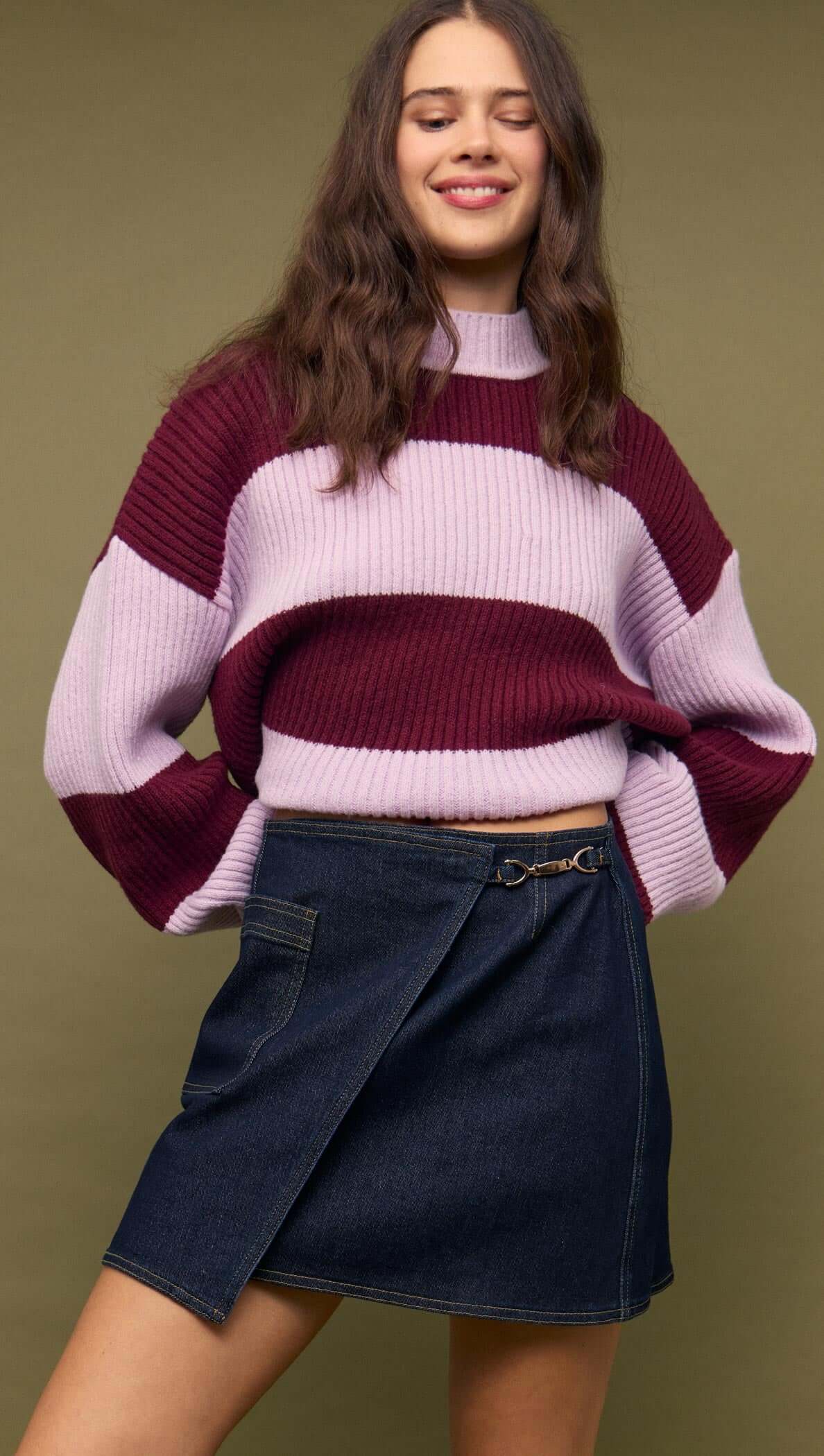 Fashionable model wearing a Denim Mini Wrap Skirt With Buckle Detail paired with a striped sweater.