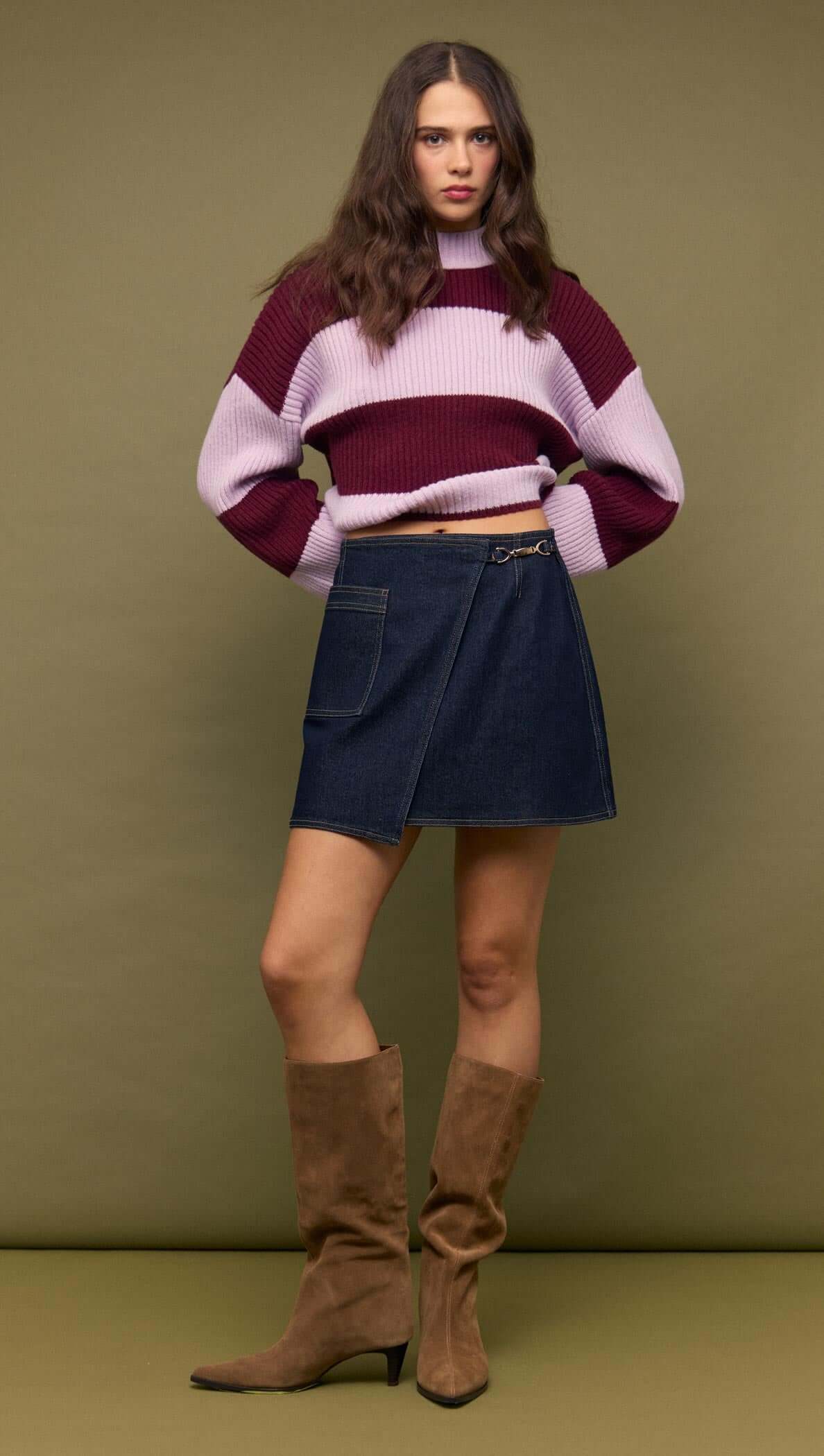 Model wearing Denim Mini Wrap Skirt With Buckle Detail paired with a striped sweater and knee-high boots