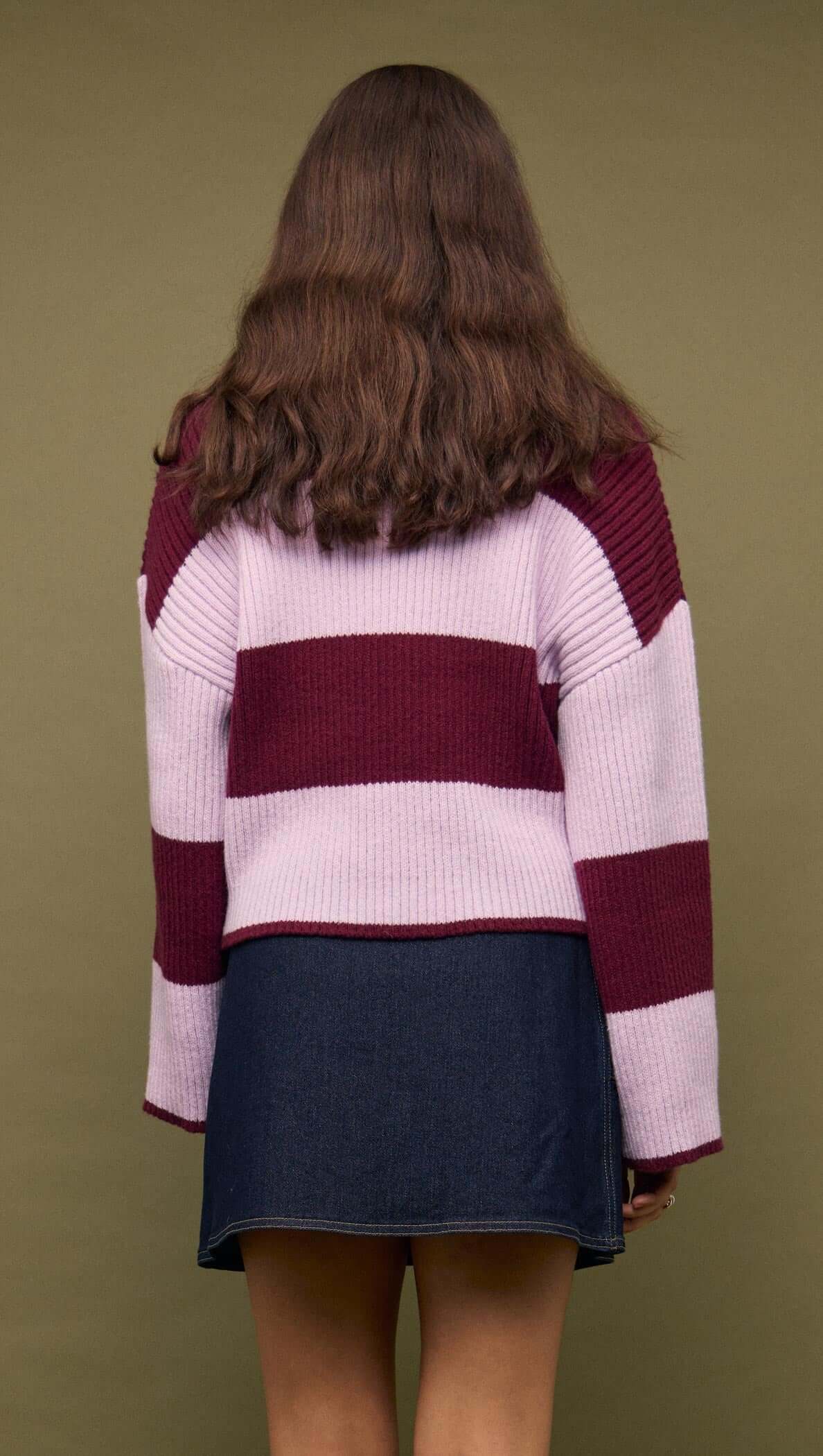 A model wearing a pink and maroon striped sweater paired with a Denim Mini Wrap Skirt With Buckle Detail, viewed from the back.