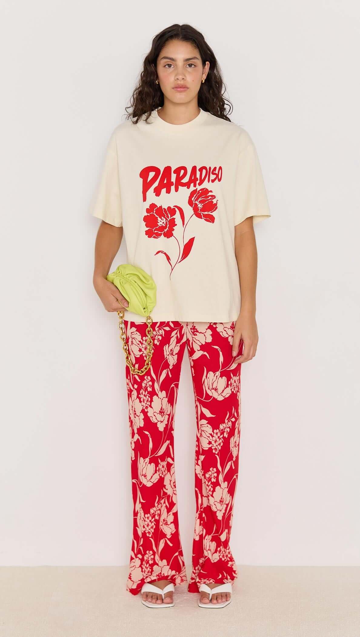 Model wearing the cream Paradiso Oversize Tee with red graphic, paired with floral red pants for a stylish off-duty look.