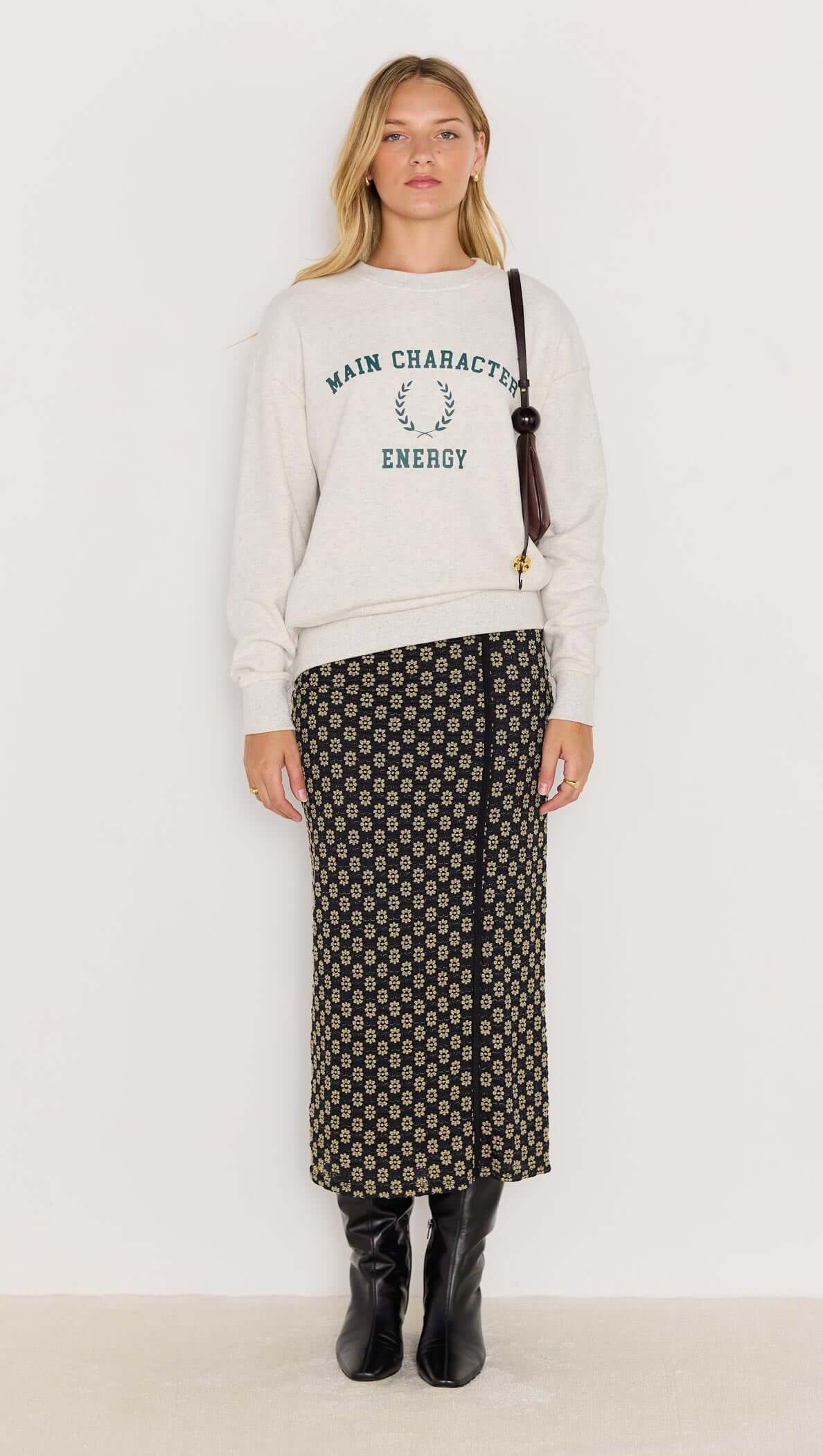 Model wearing the Energy Grey Marle Sweater featuring 'Main Character Energy' print with floral skirt and black boots.