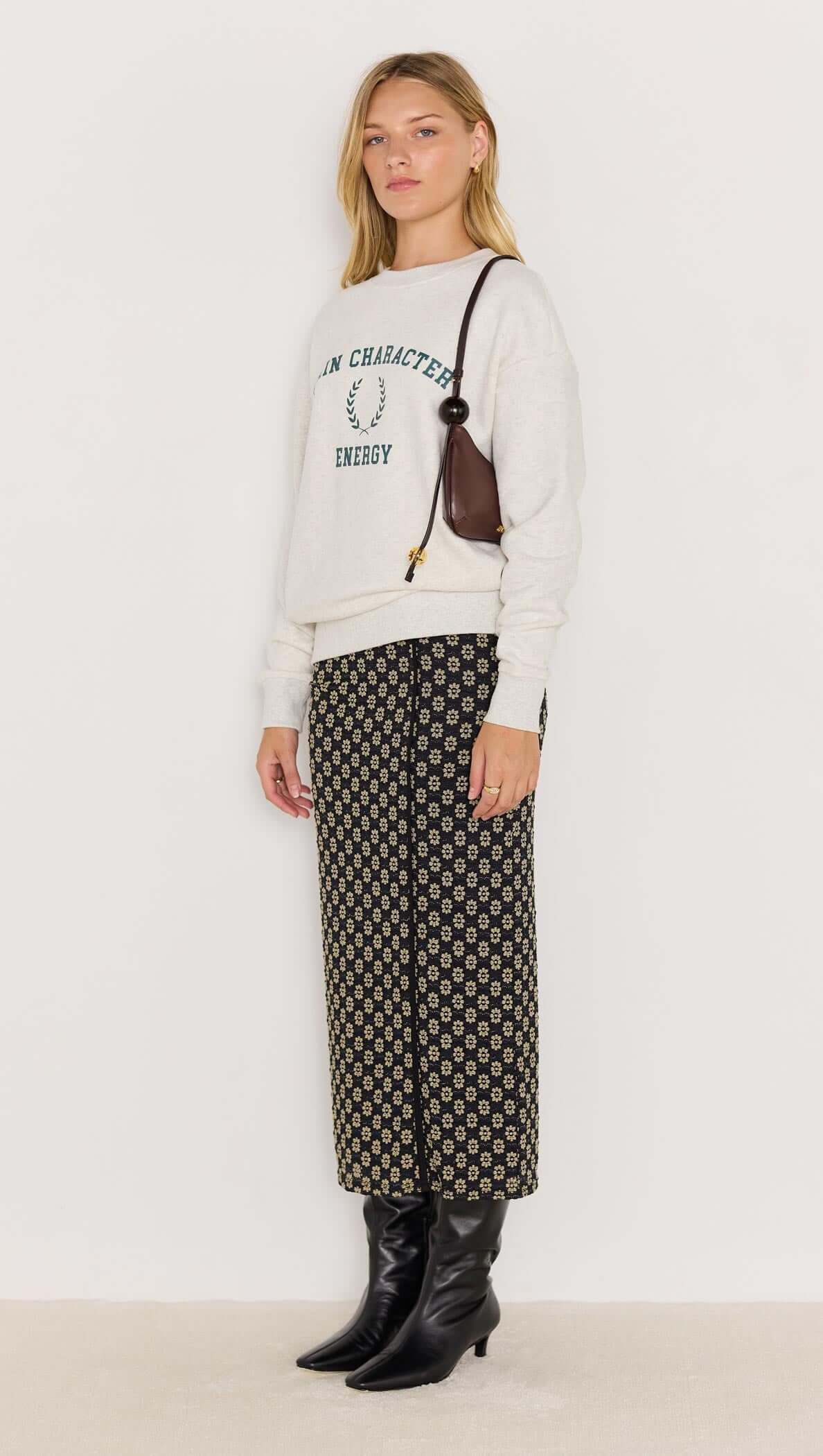 Model wearing Energy Grey Marle Sweater with collegiate graphic, paired with patterned pants and stylish boots.