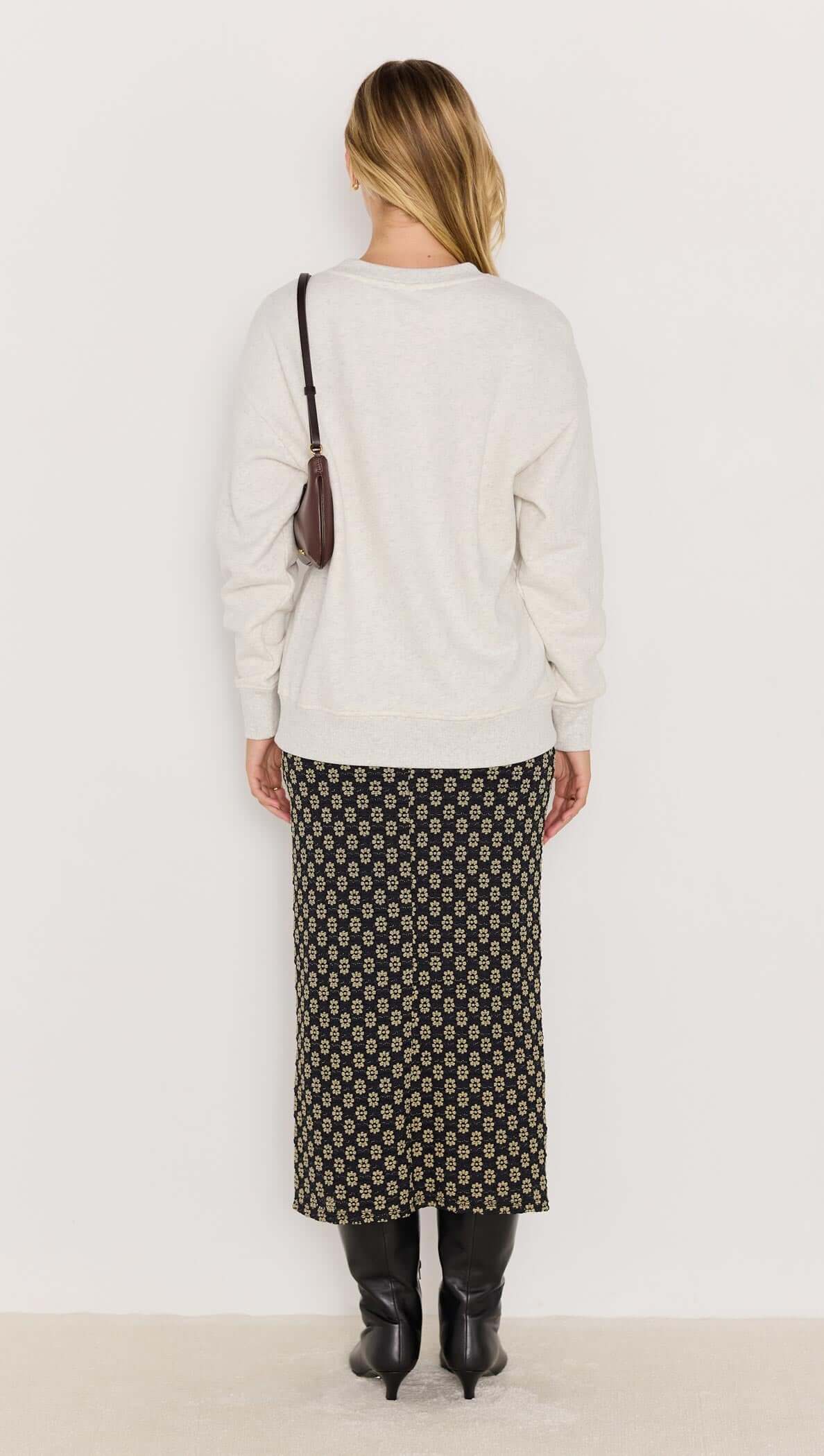 Back view of a woman in a light marle sweater and patterned skirt, showcasing a relaxed fit and stylish ensemble.