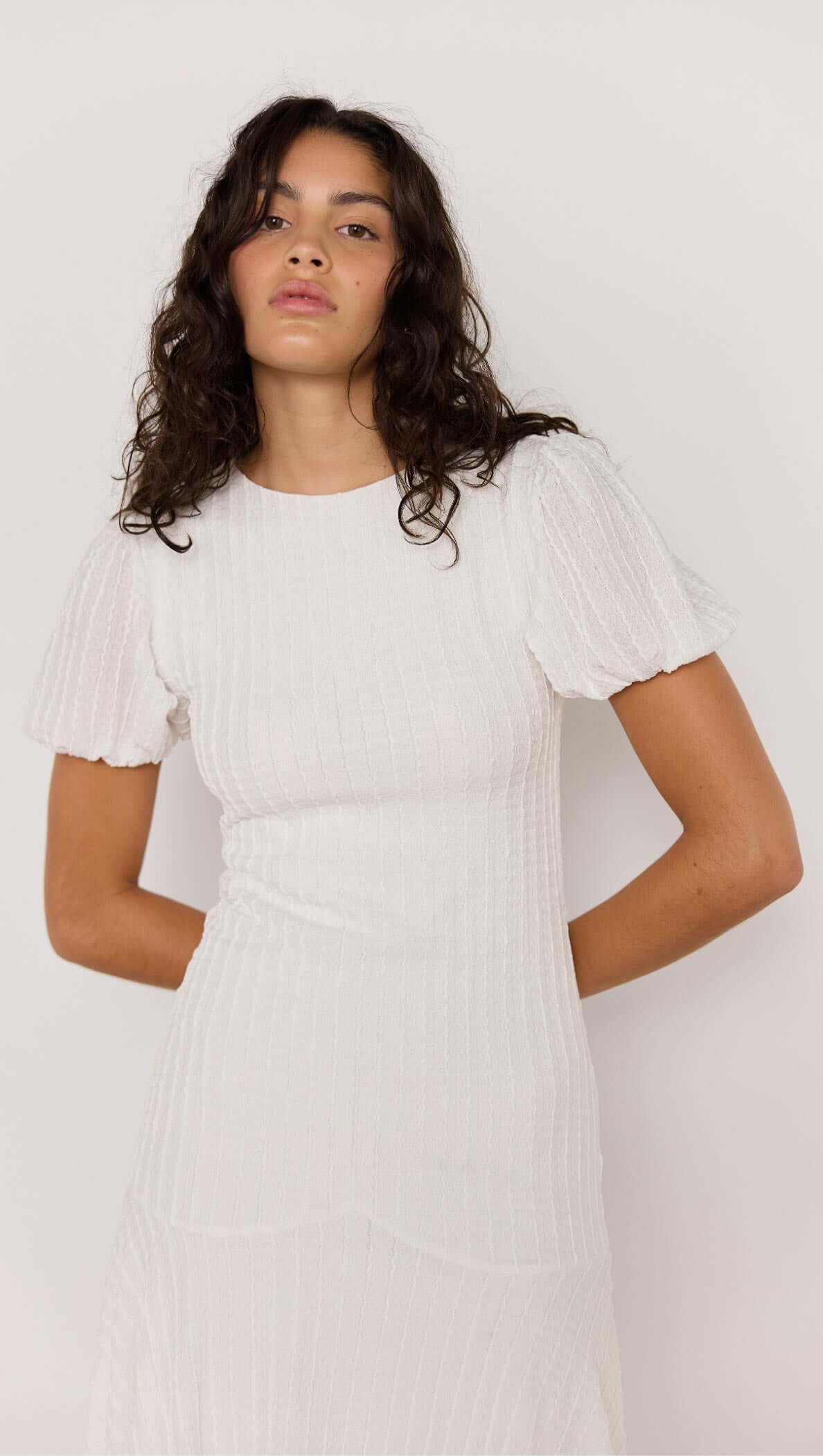 Model wearing the elegant Anais Drop Waist Midi Dress in white, showcasing puff sleeves and subtle shimmer texture.