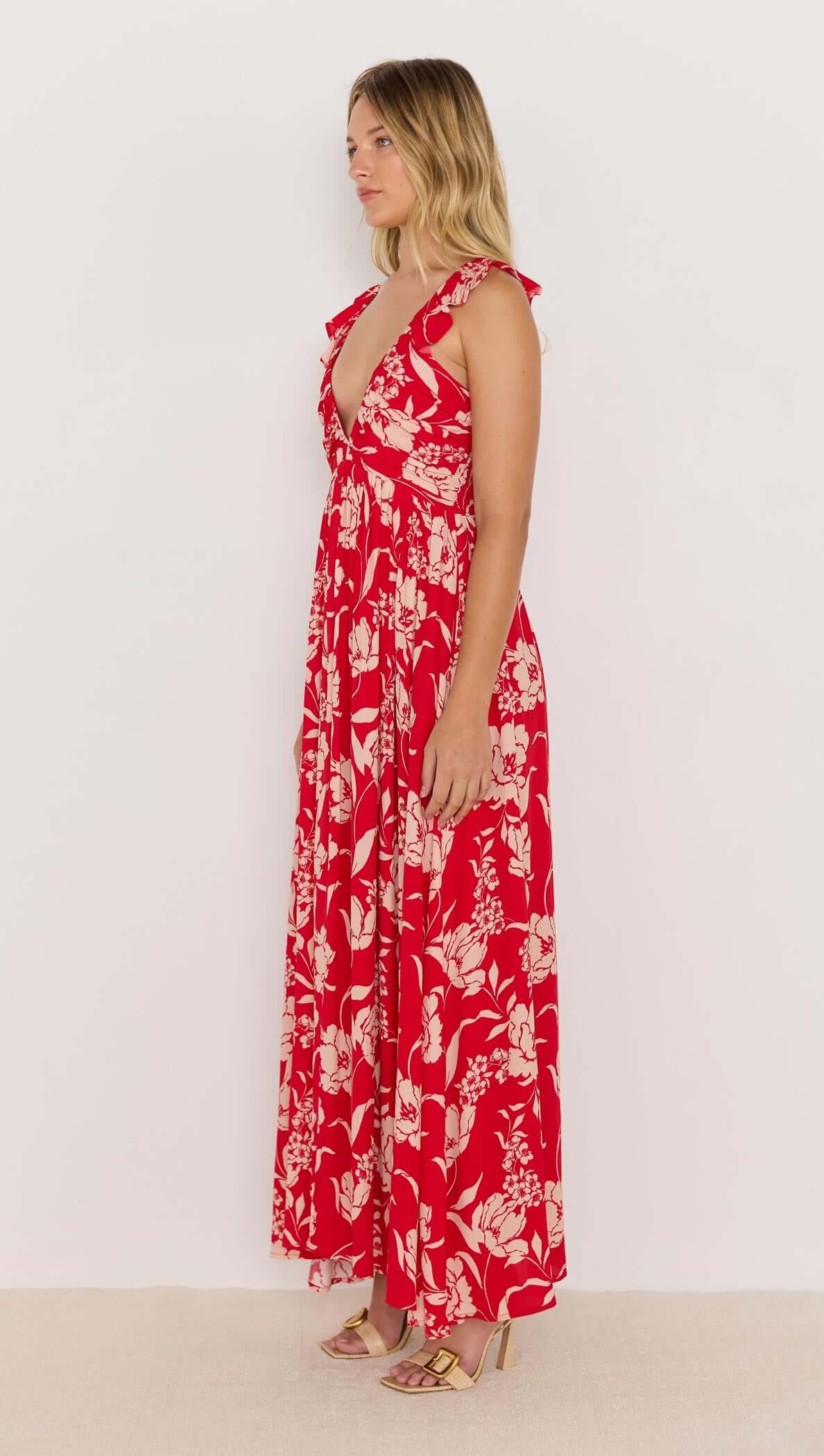 Side view of a model wearing the Poppy Maxi Dress in red floral print, featuring ruffle straps and a deep V neckline.
