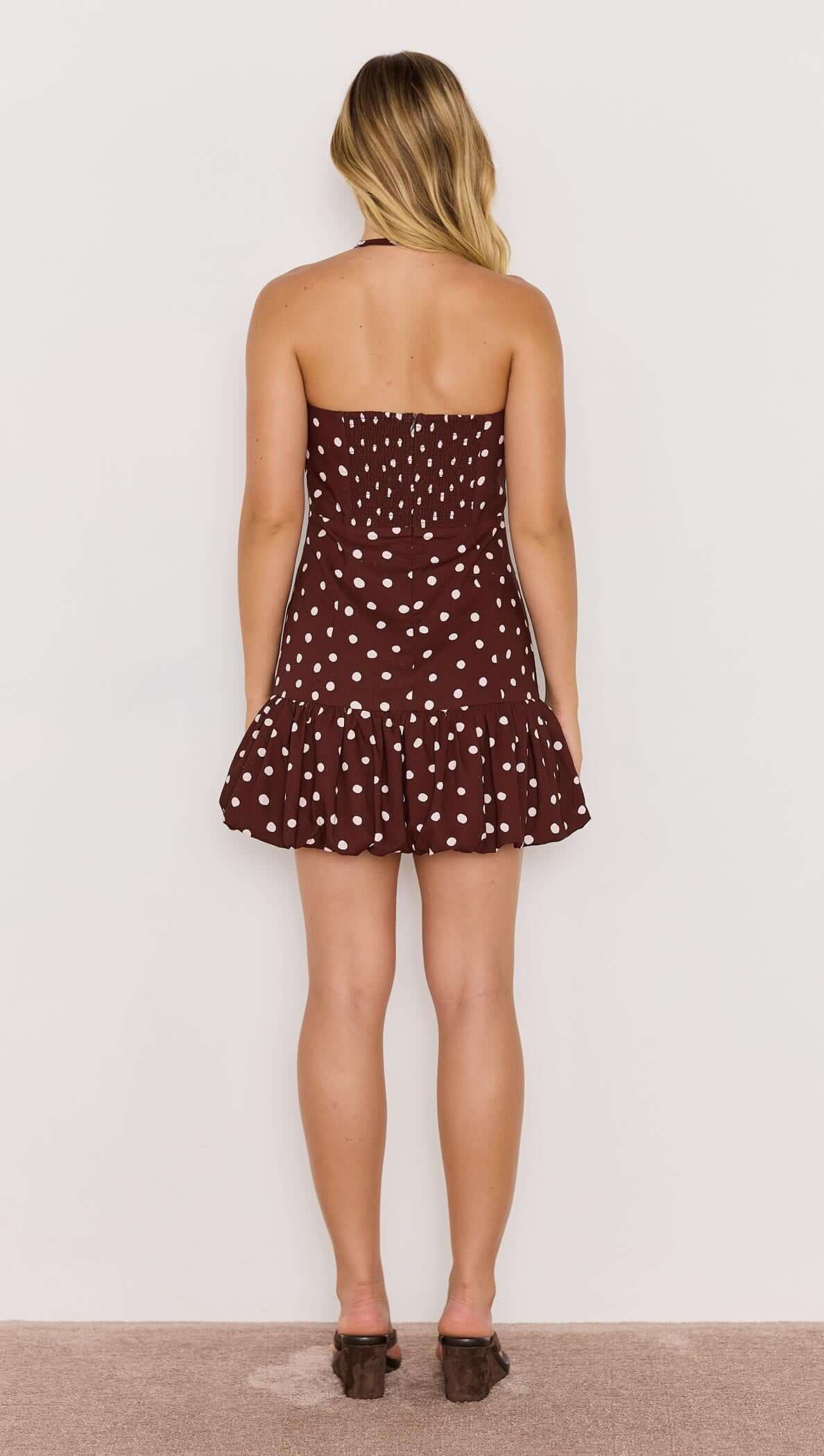 Model showing the back of the Cedar Bubble Mini Dress featuring a chocolate polka dot print and playful bubble hem.