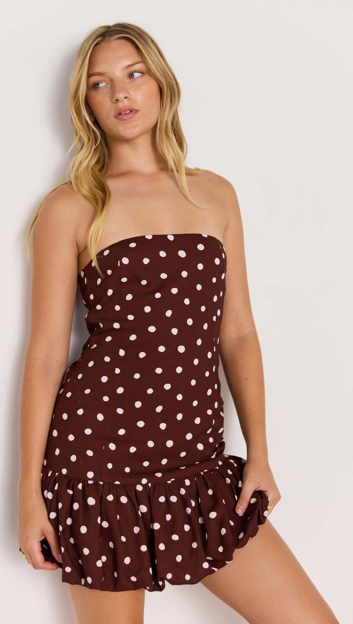 Model wearing the Cedar Spot Bubble Mini Dress, featuring a strapless design, chocolate brown with white polka dots, and playful bubble hem.