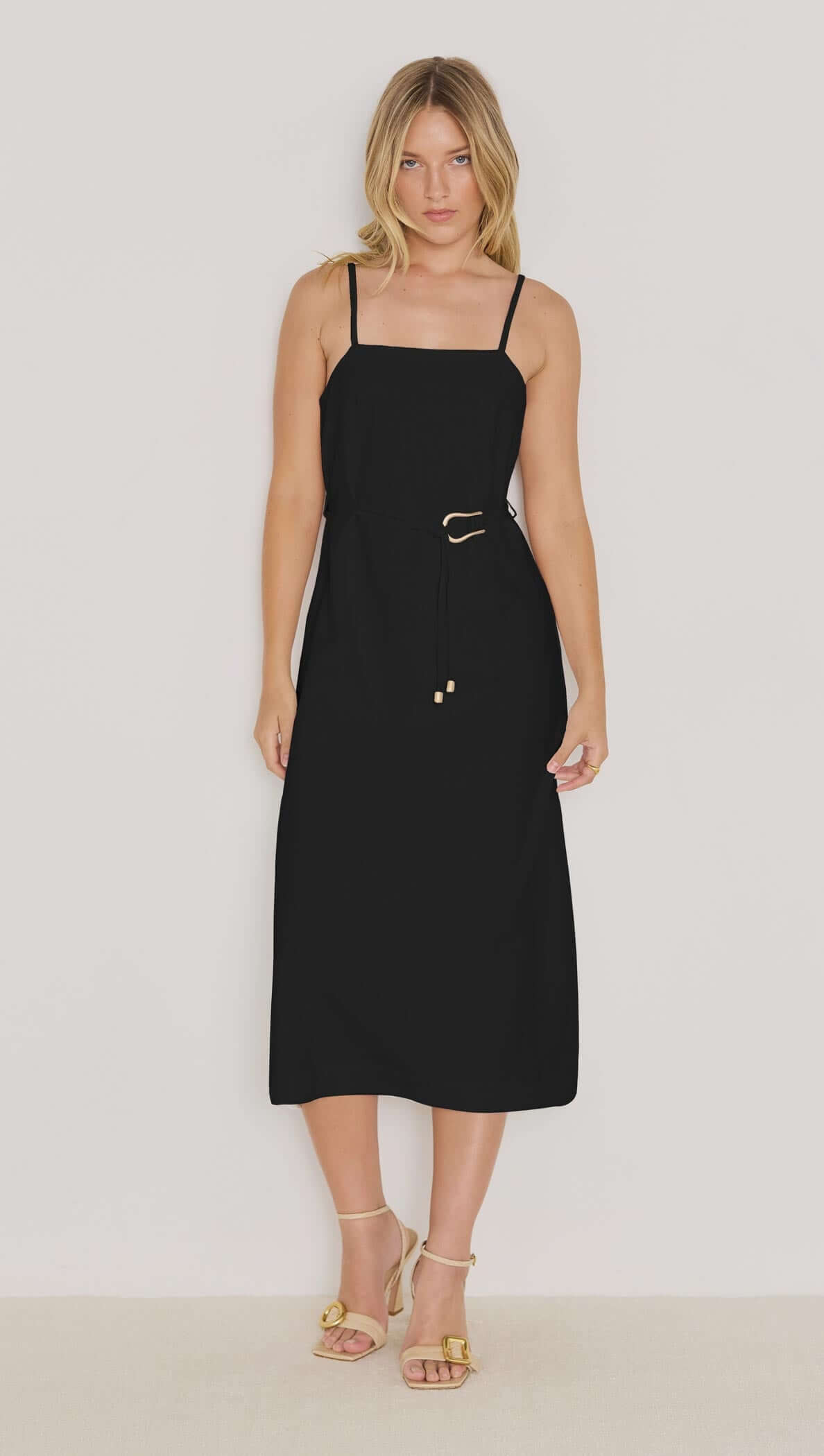Model wearing the Irena Belted Sundress in black featuring a square neckline, slim straps, and a gold-tone buckle.