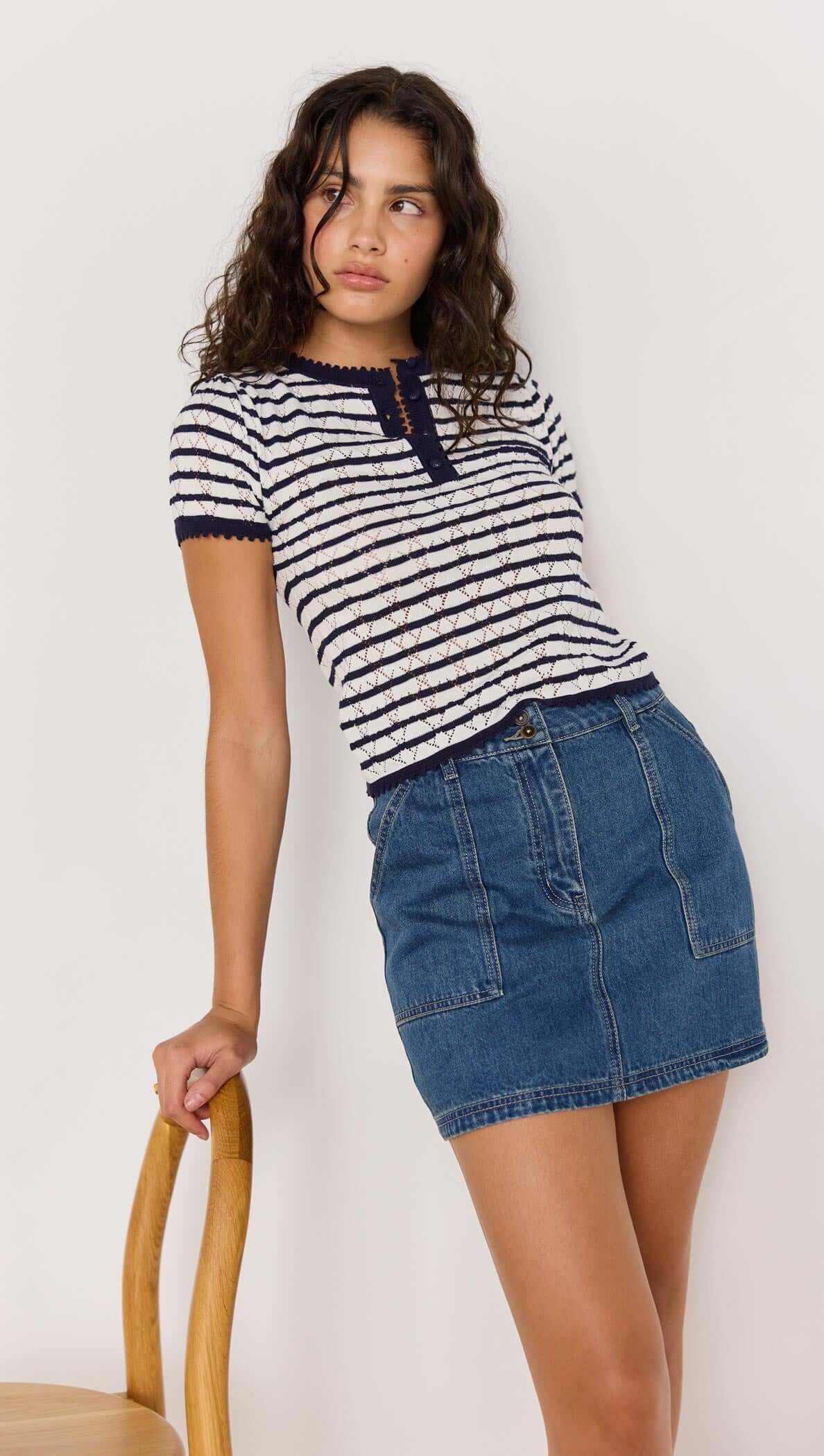 Model wearing navy and white striped CHLOE STRIPE KNIT TEE with short sleeves and a Henley neckline, paired with a denim skirt.
