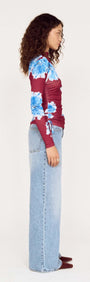 Side view of a model wearing a blue floral mesh long sleeve top paired with light blue jeans.