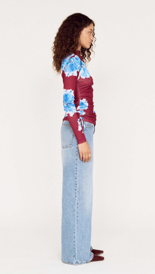Side view of a model wearing a blue floral mesh long sleeve top paired with light blue jeans.
