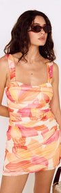 Model wearing a Sunset Leaf Print Gathered Mini Dress with colorful abstract print and sunglasses.