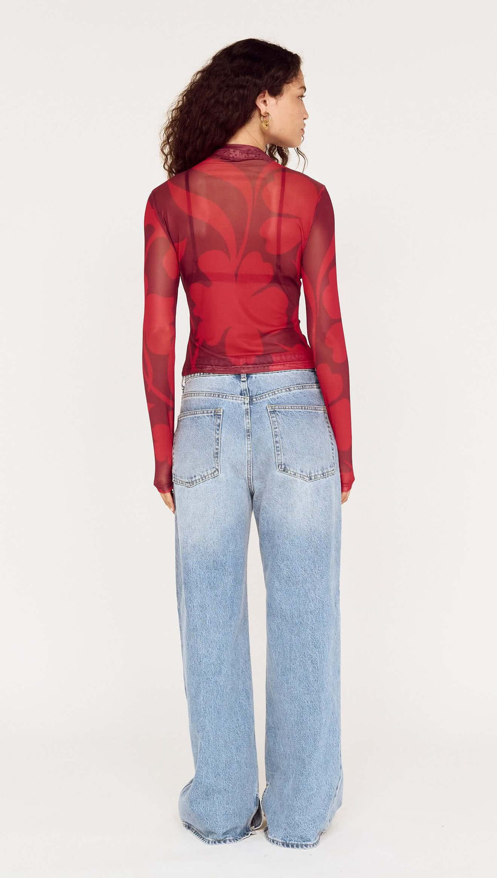 Back view of a model wearing an Oversized Floral High Neck Mesh Top paired with baggy denim jeans.