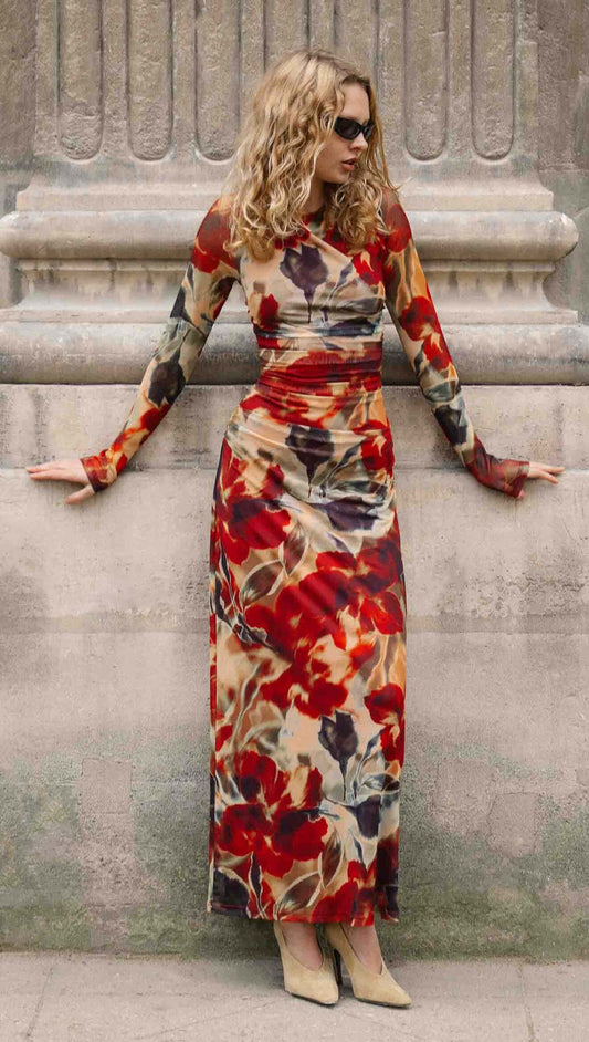 Woman in a Red Floral Sheer Mesh Midi Dress poses against a stone wall, showcasing bold floral patterns and long sleeves.