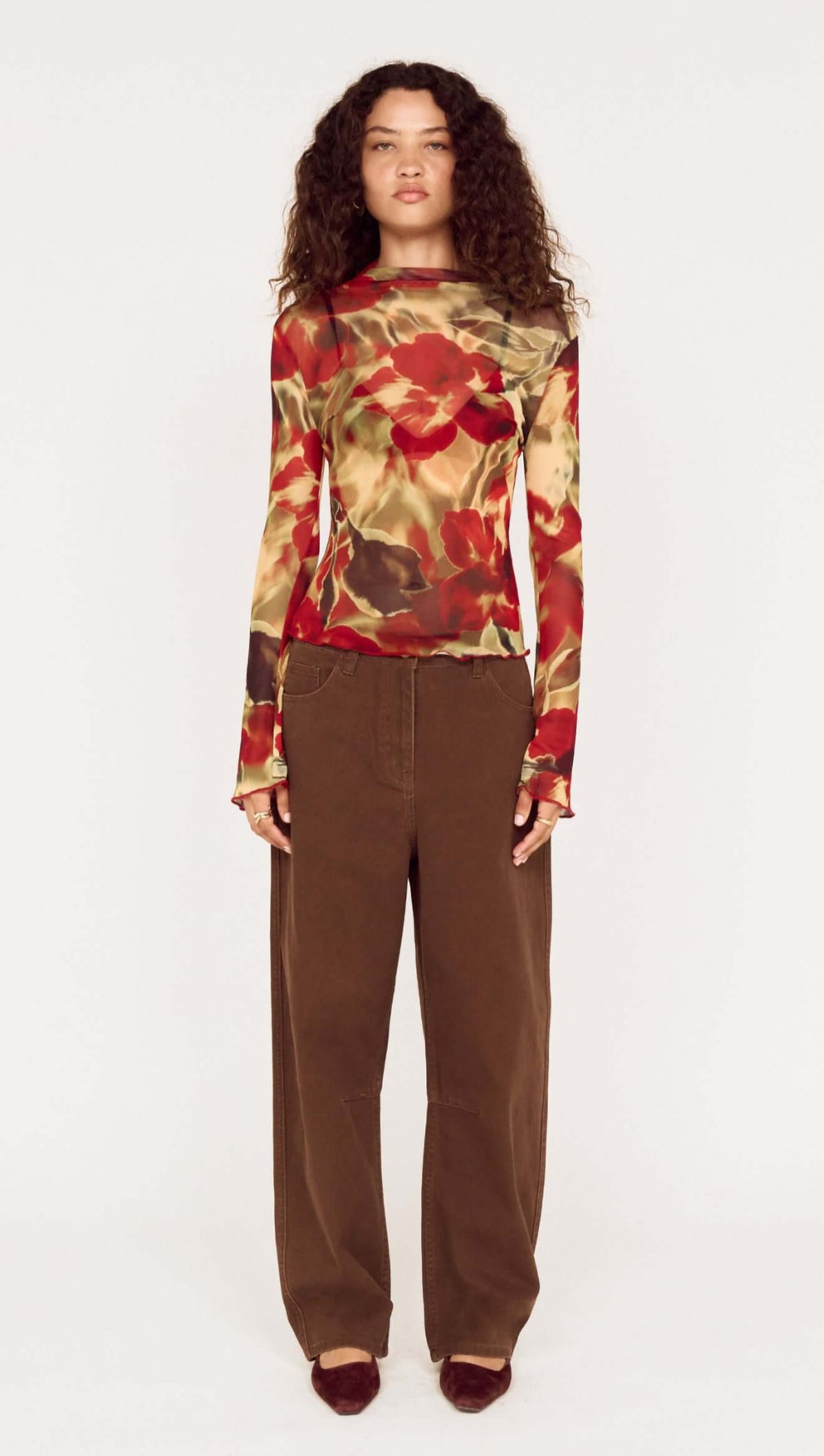 Model wearing brown mid rise barrel leg jeans with floral long-sleeve top, showcasing a modern fashion look.
