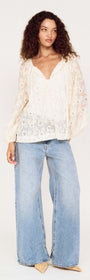 Model wearing a Cream Broderie Baloon Sleeve Blouse with jeans, showcasing its delicate lace and romantic style.