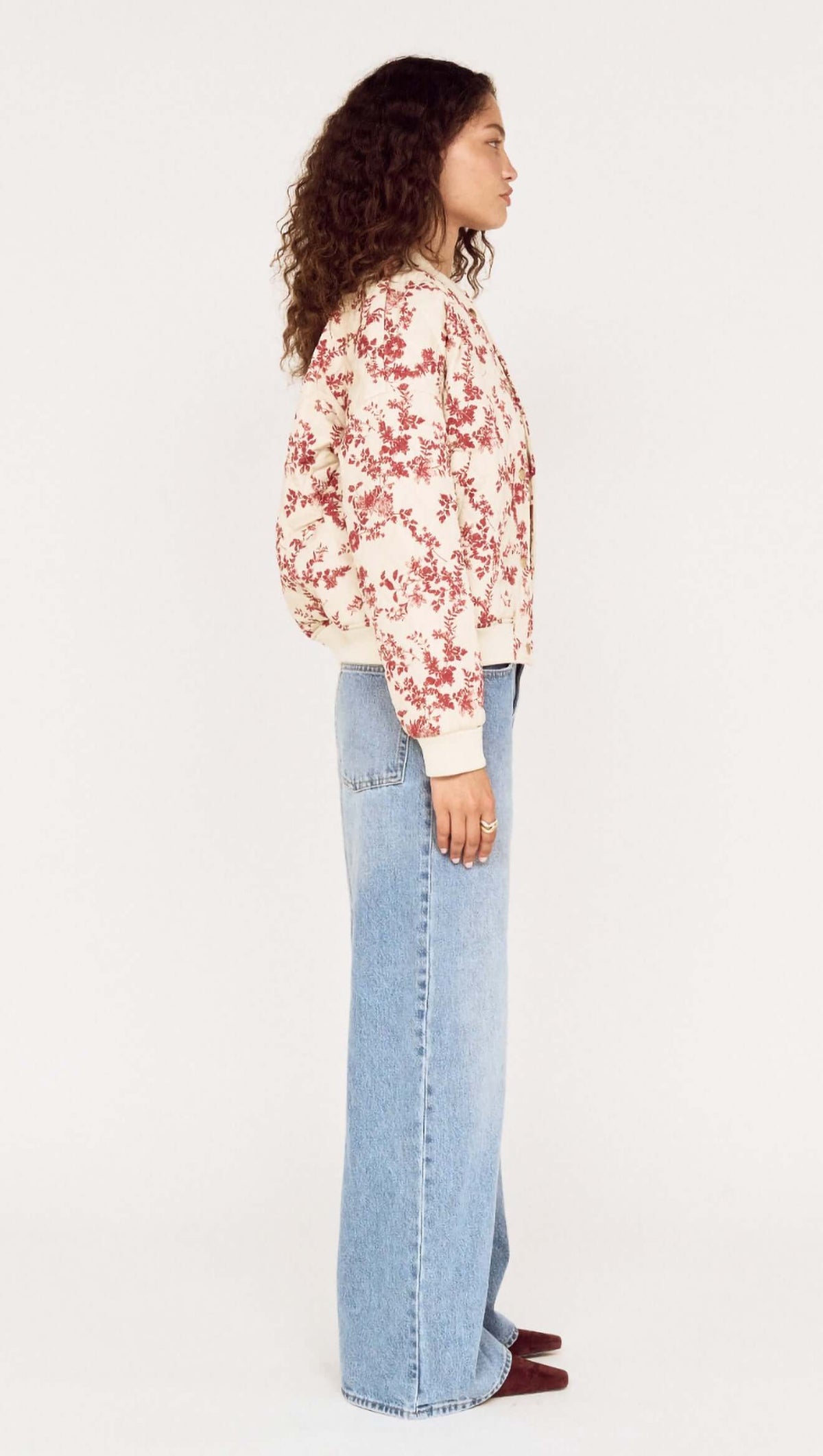 Side view of a model wearing an Autumn Floral Quilted Puffer Jacket with light blue jeans.