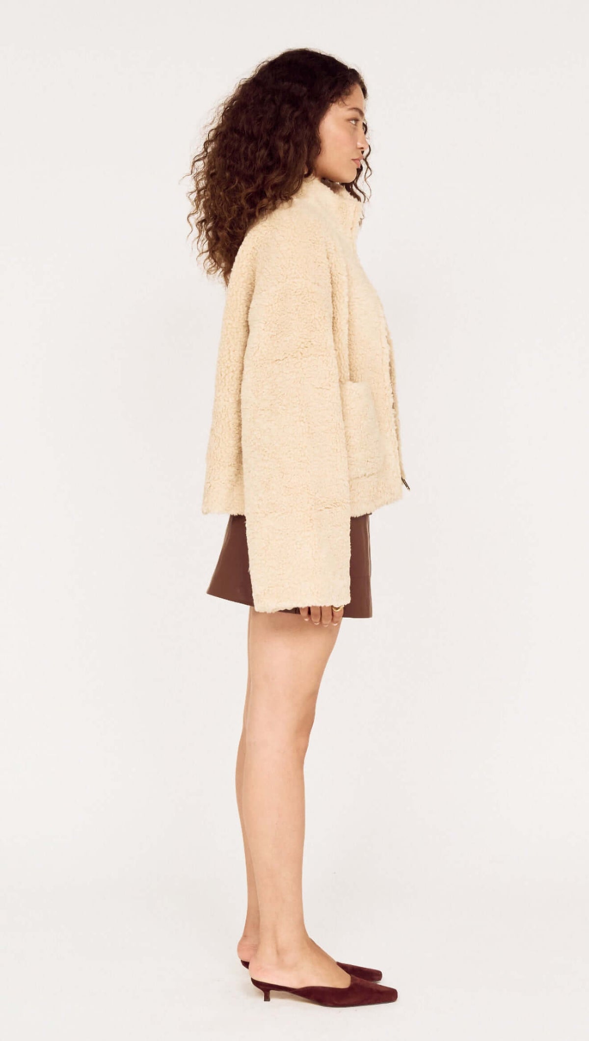 Woman wearing a Beige Teddy Jacket with High Collar, styled with a brown mini skirt and slip-on shoes.