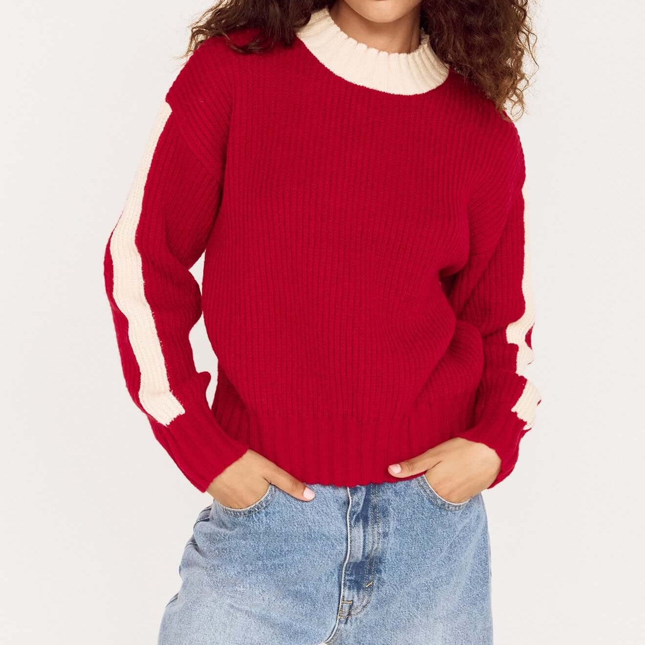 A model wearing a relaxed red contrast stripe jumper with cream detailing, styled with light denim pants.
