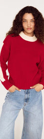 A model wearing a relaxed red contrast stripe jumper with cream detailing, styled with light denim pants.