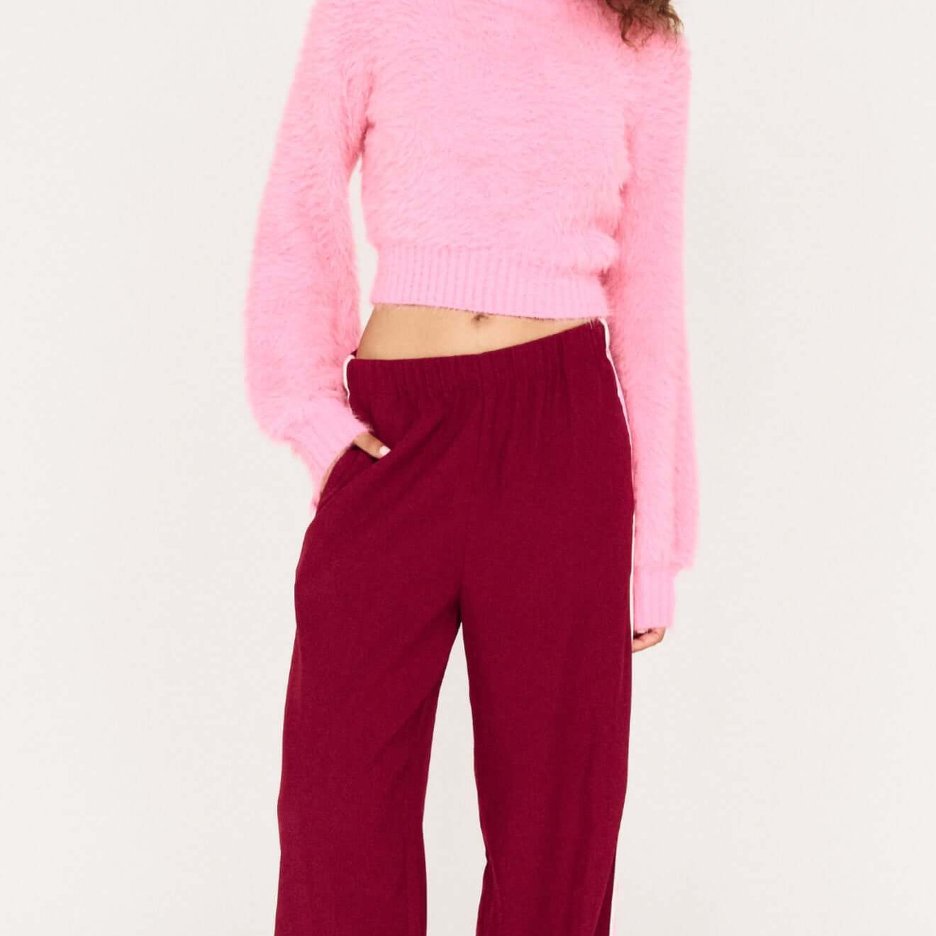 Model wearing the Clio Cropped Fuchsia Pink Fluffy Jumper with wide-leg pants, showcasing a stylish and cozy outfit.