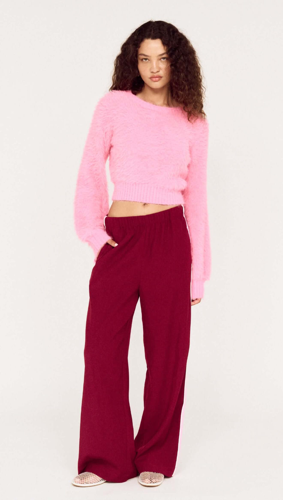 Model wearing the Clio Cropped Fuchsia Pink Fluffy Jumper with wide-leg pants, showcasing a stylish and cozy outfit.