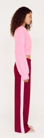 Side view of a model wearing the Clio Cropped Fuchsia Pink Fluffy Jumper with burgundy pants featuring a pink stripe.