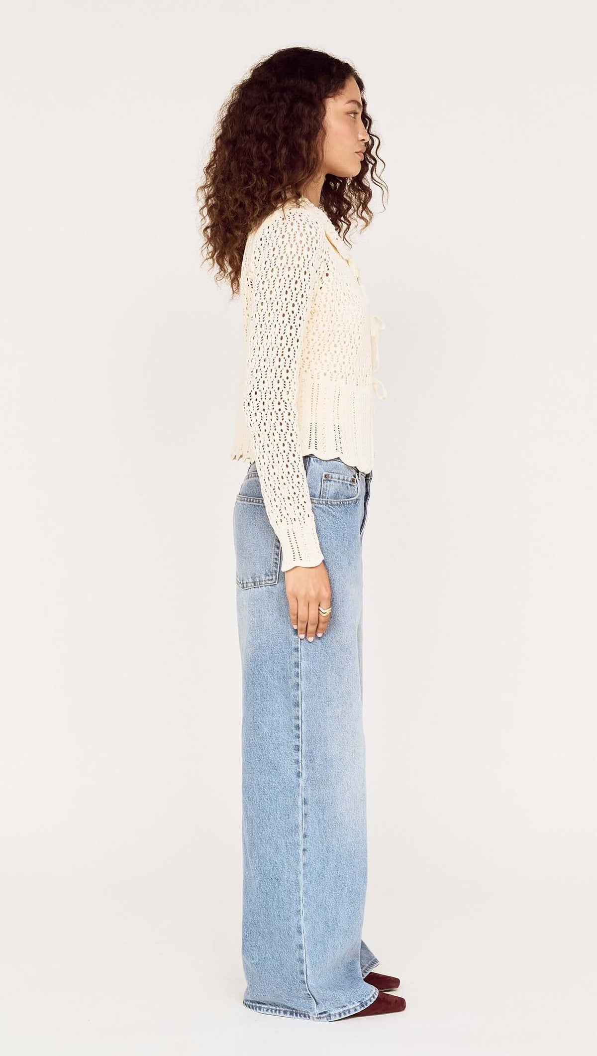 Model wearing a Cream Pointelle Knit Cardi with Tie Front, showing side view, paired with loose-fitting jeans.