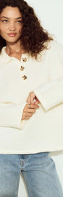 Woman wearing a Gold Detail Relaxed Polo Knit in cream color, featuring a collar and decorative buttons, styled with jeans.