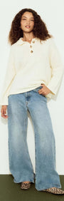 Woman wearing a Gold Detail Relaxed Polo Knit with wide-leg jeans and stylish shoes, showcasing a relaxed and fashionable look.