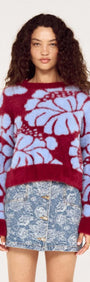 Model wearing Intarsia Floral Soft Touch Jumper in red and blue with floral design paired with a denim skirt.