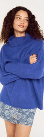 Model wearing a Blue Oversized Roll Neck Jumper, styled casually with a denim mini skirt.