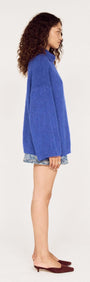 Side view of a model wearing a Blue Oversized Roll Neck Jumper with denim shorts and stylish shoes.