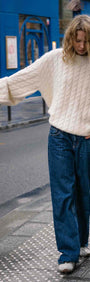 Cream Relaxed Fit Cable Knit Jumper styled with wide-leg jeans in a city street setting.