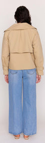 Back view of a woman wearing a Beige Cotton Drill Cropped Trench with wide lapels and loose blue jeans.