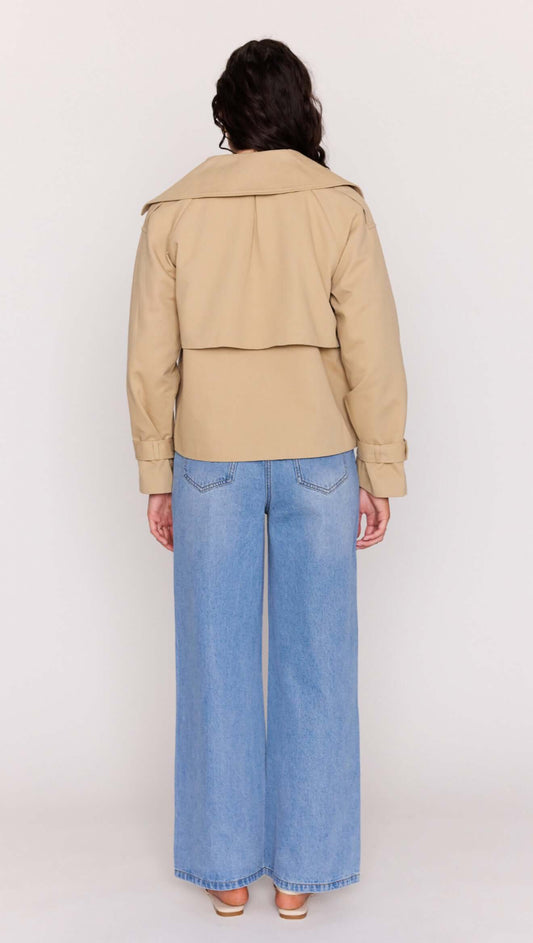 Back view of a woman wearing a Beige Cotton Drill Cropped Trench with wide lapels and loose blue jeans.