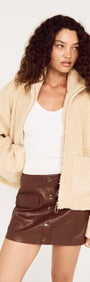 Beige Teddy Jacket with High Collar worn by a model with curly hair and a white top, paired with a brown leather skirt.