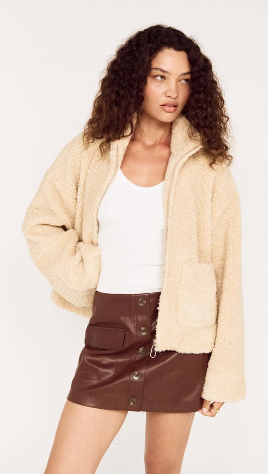 Beige Teddy Jacket with High Collar worn by a model with curly hair and a white top, paired with a brown leather skirt.