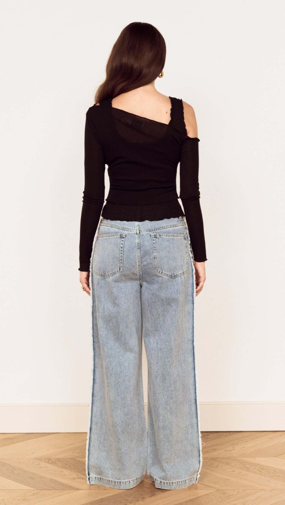 Back view of model wearing Black Asymmetric Layered Mesh Top paired with wide-leg jeans.