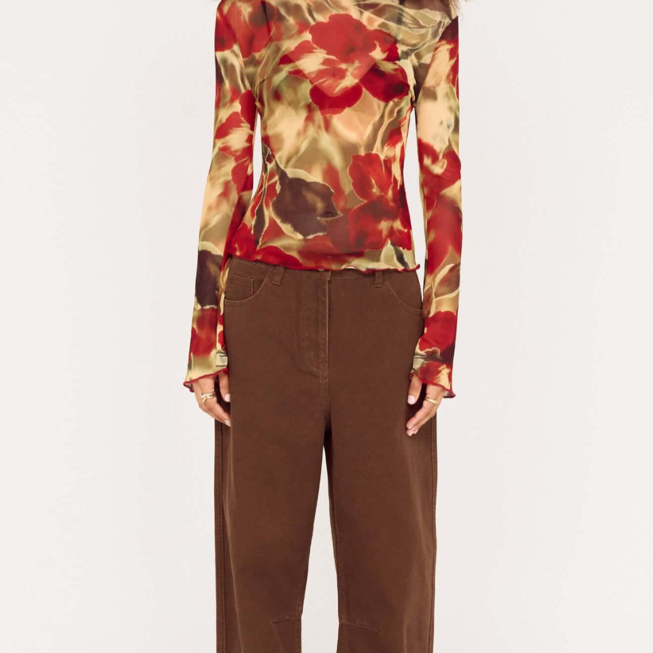 Model wearing brown mid rise barrel leg jeans with floral long-sleeve top, showcasing a modern fashion look.