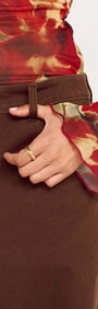 Close-up of a person wearing Brown Mid Rise Barrel Leg Jeans, showing hand on waistband with floral long-sleeve top.