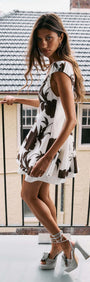 A model wearing a Brown and Cream Floral Layered Mini Dress on a balcony, showcasing floral design and stylish heels.
