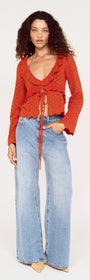 Model wearing a burnt orange pointelle tie front top paired with light blue wide-leg jeans.