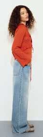 Model wearing a Burnt Orange Pointelle Tie Front Top with blue wide-leg jeans and animal print shoes.