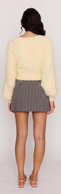 Back view of a woman wearing a Butter Yellow Fluffy Knit Jumper paired with a striped skirt.